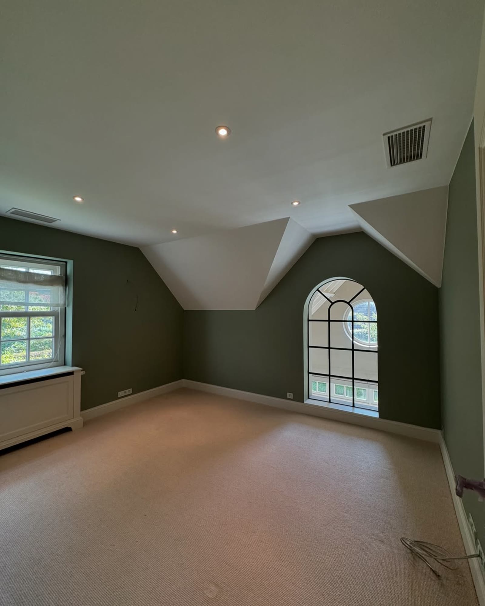 Bedroom painted deep green with a white arched window